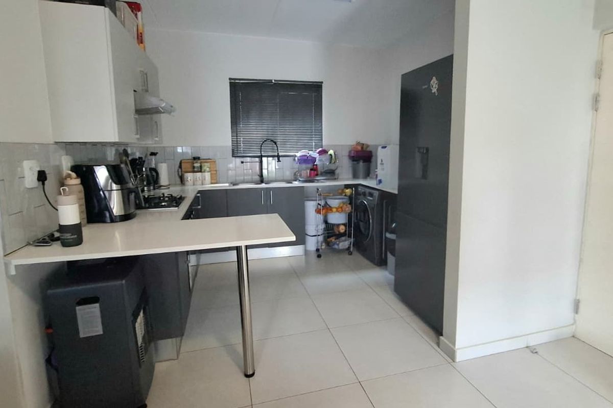 A functional kitchen featuring built-in cabinetry, a gas hob with extractor fan, tiled backsplash, and a breakfast counter, with integrated laundry appliance space.