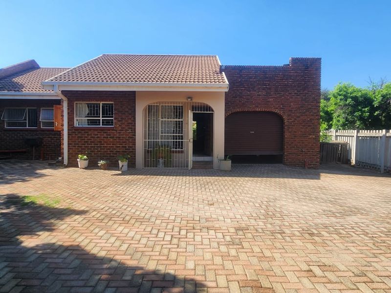 Front exterior view of a brick townhouse featuring a paved driveway, integrated garage, and secure entrance with a security gate.