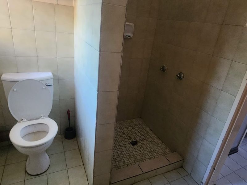 A functional bathroom featuring a toilet and a walk-in shower with tiled finishes, requiring cosmetic updates to modernize the space.