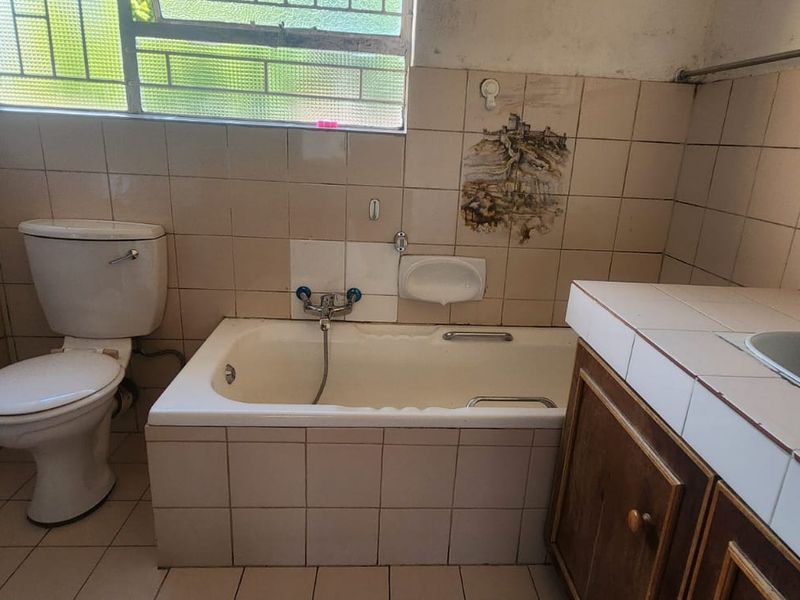 A dated bathroom featuring a bathtub, toilet, and vanity basin with tiled finishes, requiring cosmetic updates to modernize the space.