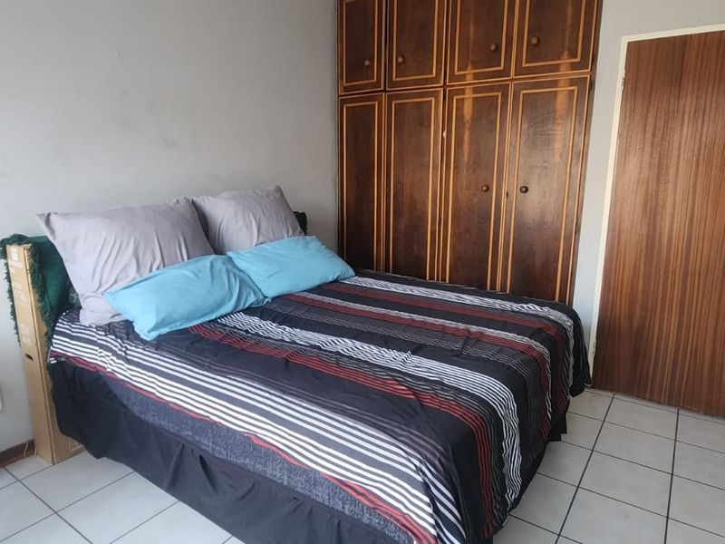 A bedroom featuring tiled flooring, built-in wooden cupboards, and a standard wooden door, offering a functional space with potential for cosmetic updates.