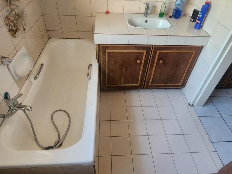 A dated bathroom featuring a built-in vanity with a ceramic basin, a standard bathtub, and tiled surfaces throughout, offering potential for modernization.