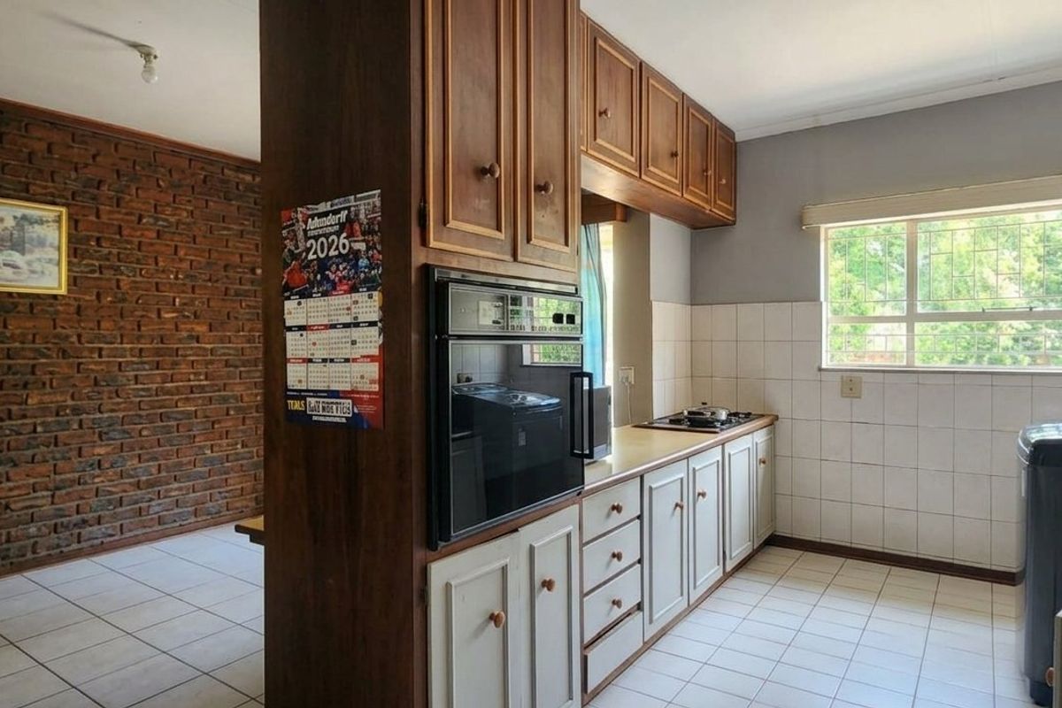 A functional kitchen featuring built-in cabinetry, an integrated oven, hob, and tiled finishes, adjacent to an exposed brick wall living area.