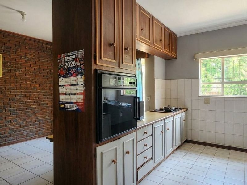 A functional kitchen featuring built-in cabinetry, an integrated oven, hob, and tiled finishes, adjacent to an exposed brick wall living area.