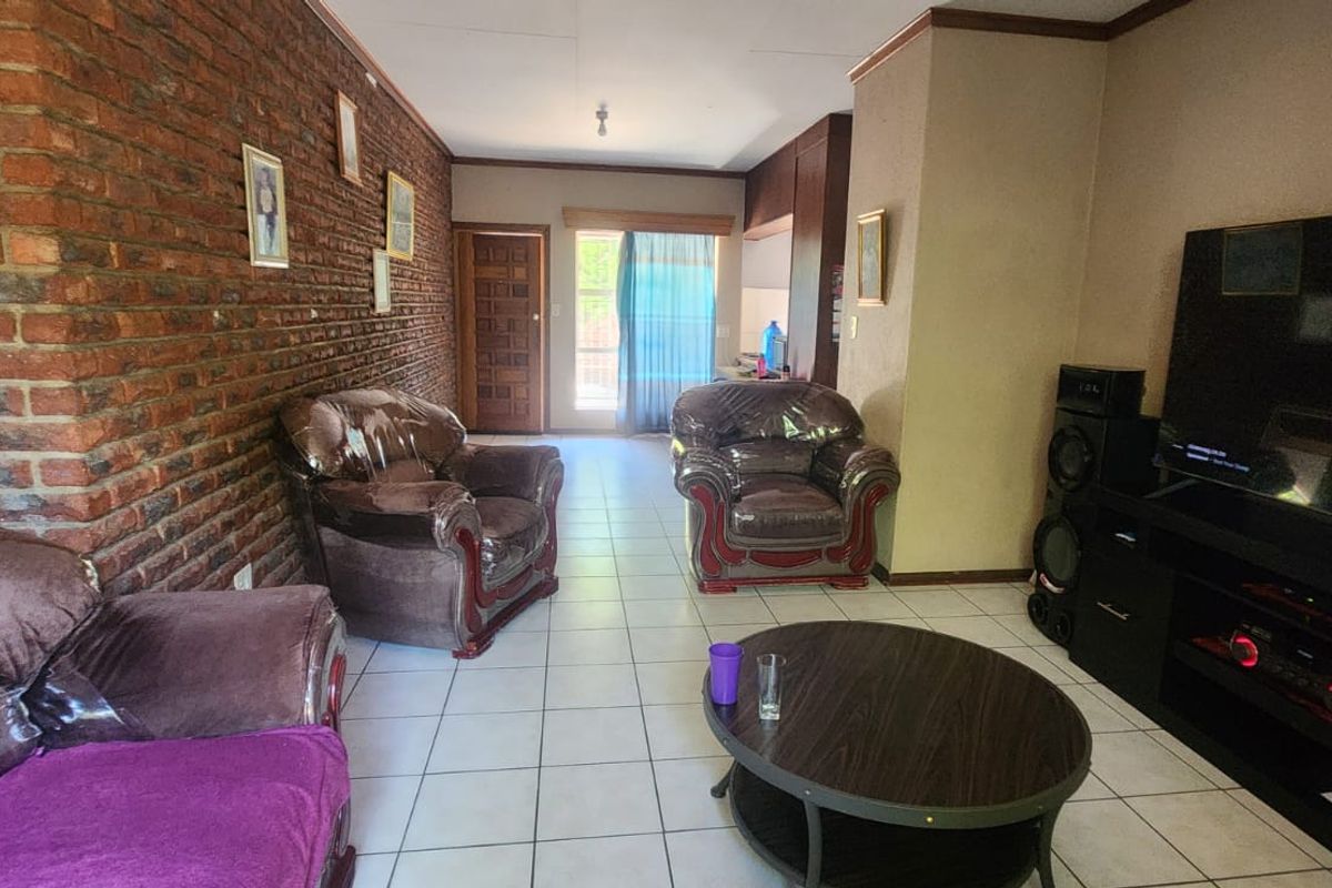 Spacious living area featuring an exposed brick wall, ceramic tiled flooring, and direct access to the outdoor area through a sliding glass door.