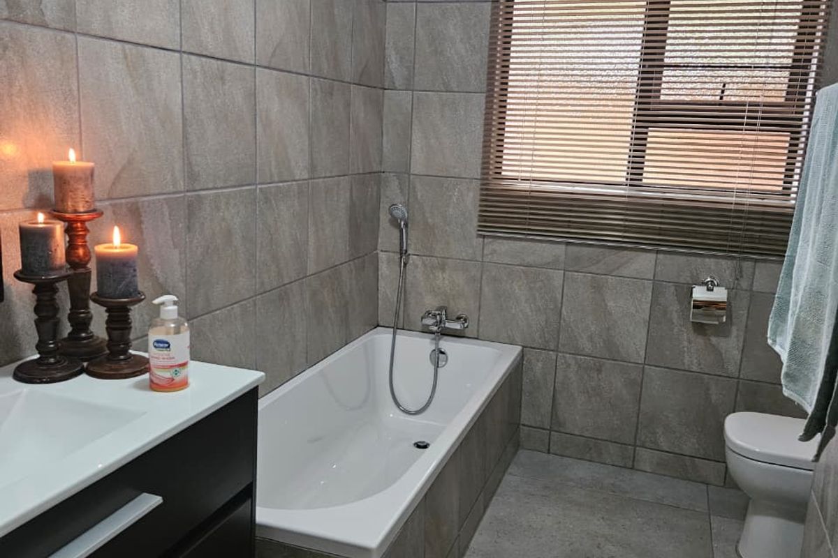 A modern bathroom featuring full-height wall tiling, a built-in vanity, a bathtub with a handheld shower mixer, and a toilet.