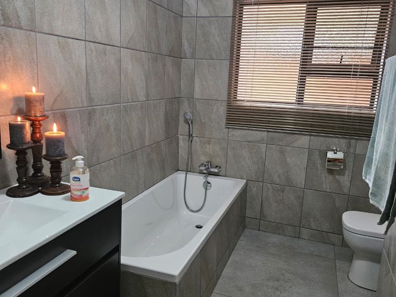 A modern bathroom featuring full-height wall tiling, a built-in vanity, a bathtub with a handheld shower mixer, and a toilet.