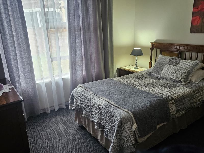 A cozy bedroom featuring carpeted flooring and a large sliding window that allows for natural light.