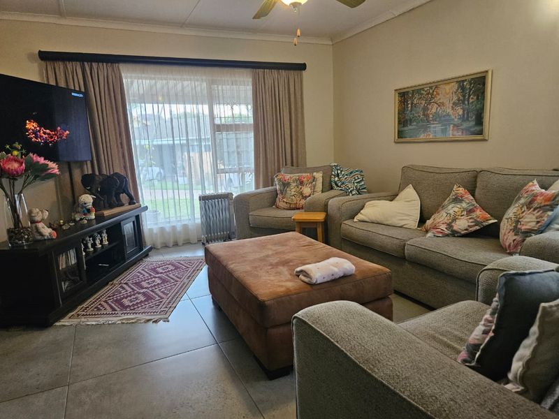 A comfortable living room featuring large sliding glass doors, tiled flooring, and a ceiling fan, providing a functional and well-lit space.