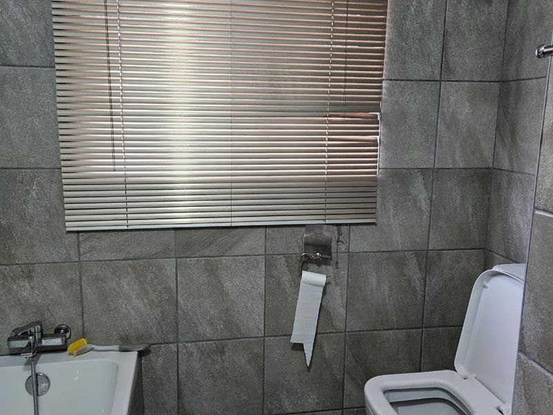 A functional bathroom featuring full-height wall tiling, a standard bathtub with shower mixer, and a toilet.