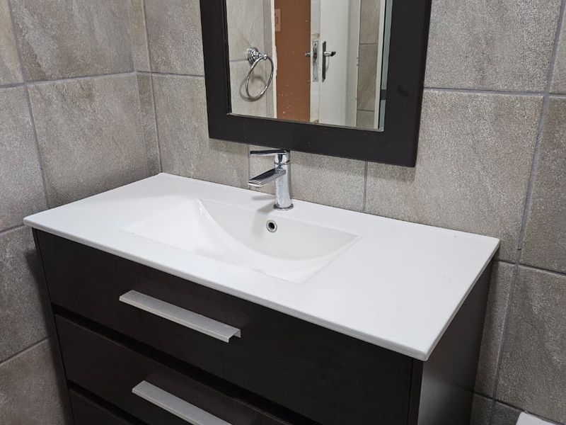 A modern bathroom vanity featuring a dark wood cabinet, white basin, chrome mixer tap, and a matching framed wall mirror against tiled walls.