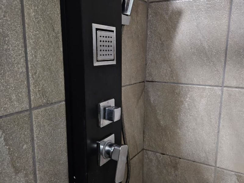 Close-up view of a modern black shower panel system installed against neutral ceramic wall tiles in a bathroom.