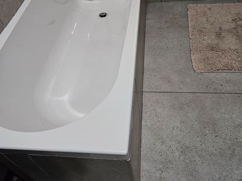 A functional bathroom featuring a built-in bathtub with a handheld shower mixer, complemented by neutral-toned floor and wall tiling.