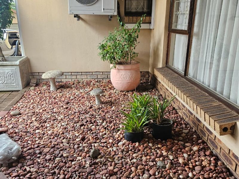 A covered patio area featuring a pebble-covered ground surface, brick detailing, and a wall-mounted air conditioning unit.