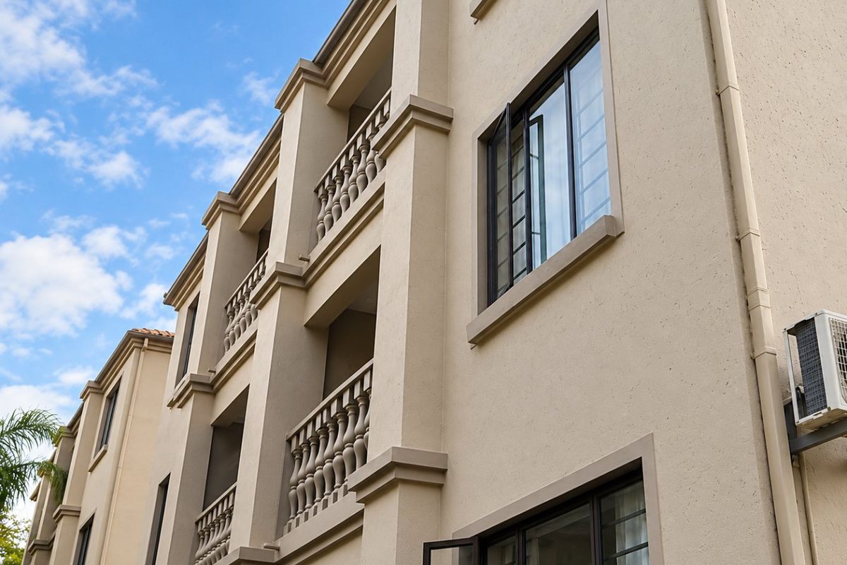 Exterior view of an apartment building facade featuring multiple balconies with decorative balustrades, casement windows with security bars, and an external air conditioning unit.