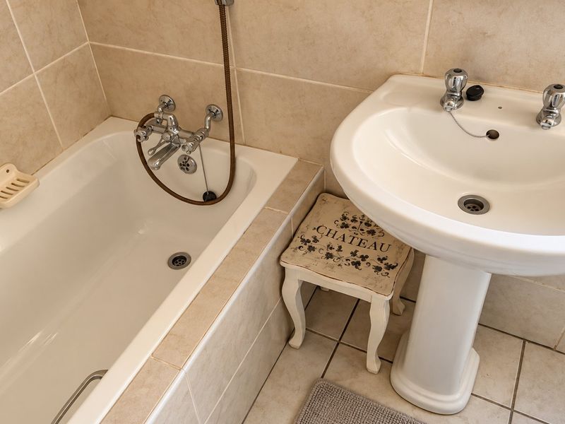 A functional bathroom featuring a white pedestal washbasin and a bathtub with a shower mixer, finished with neutral ceramic wall and floor tiles.