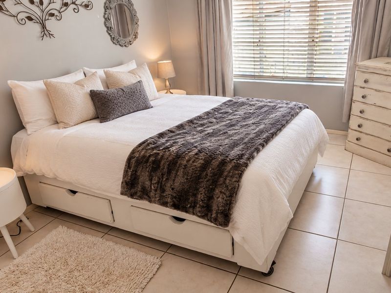 A well-maintained bedroom featuring neutral tiled flooring and venetian blinds, offering a clean and comfortable living space.