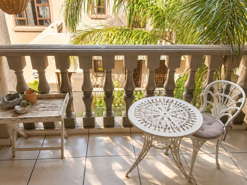 A covered balcony featuring a classic balustrade, tiled flooring, and safety netting, overlooking a residential courtyard area.
