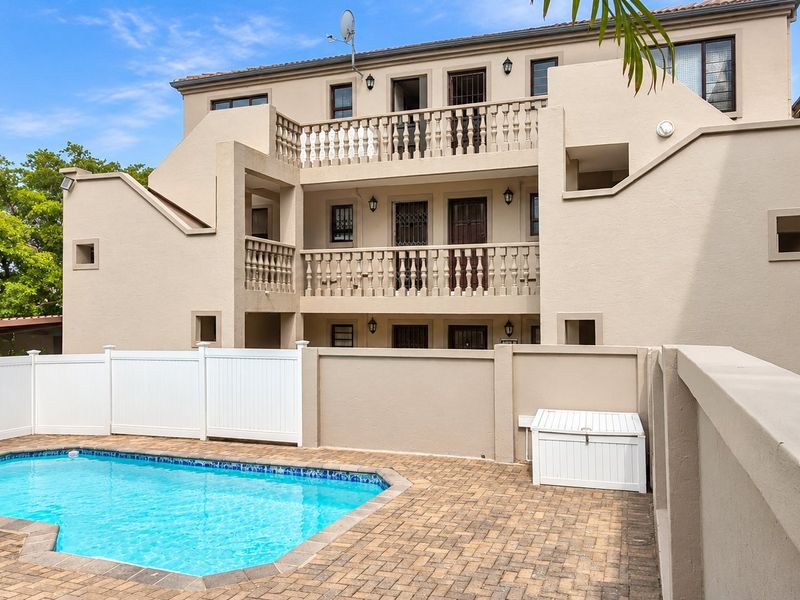 A well-maintained apartment complex exterior featuring a private swimming pool, paved deck area, and multi-level balconies with classic balustrade detailing.