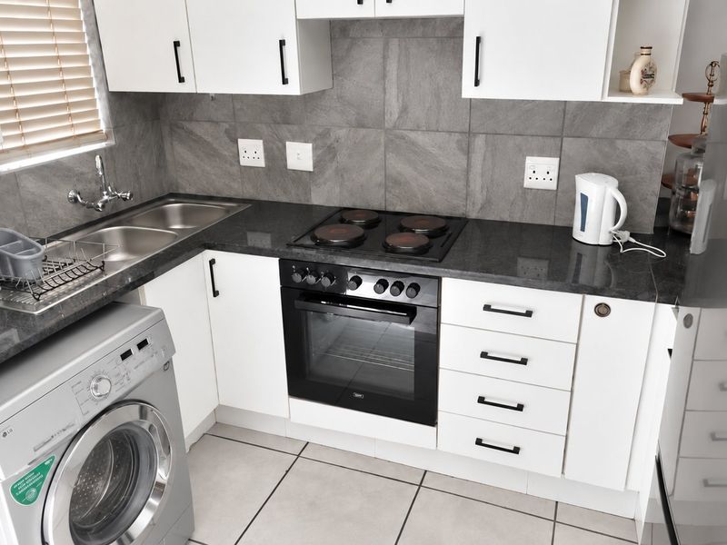 Modern kitchen featuring white cabinetry, dark stone countertops, integrated electric oven and hob, tiled backsplash, and dedicated space for laundry appliances.