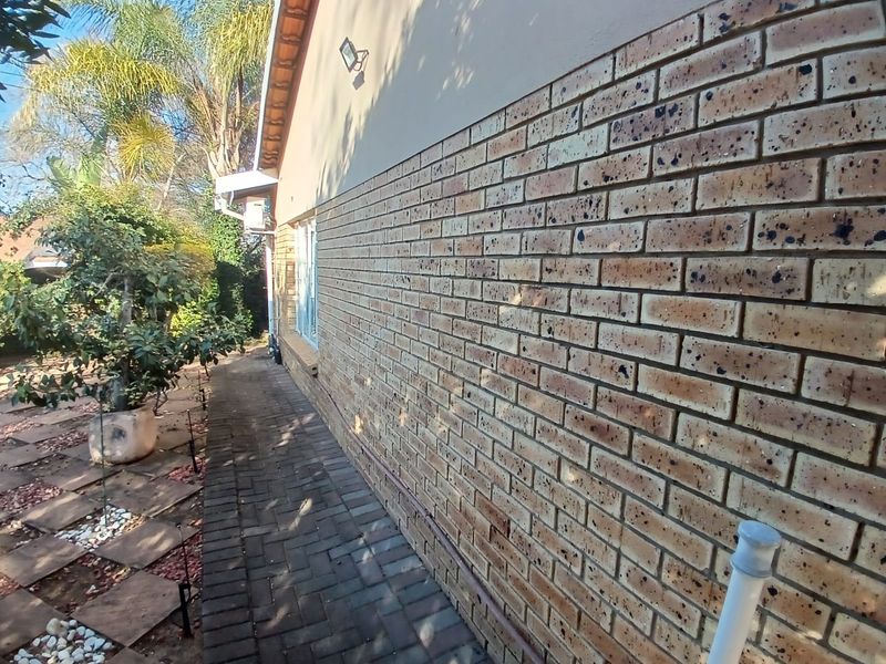 A side view of the property featuring a face brick exterior wall, a paved walkway, and established garden surroundings.