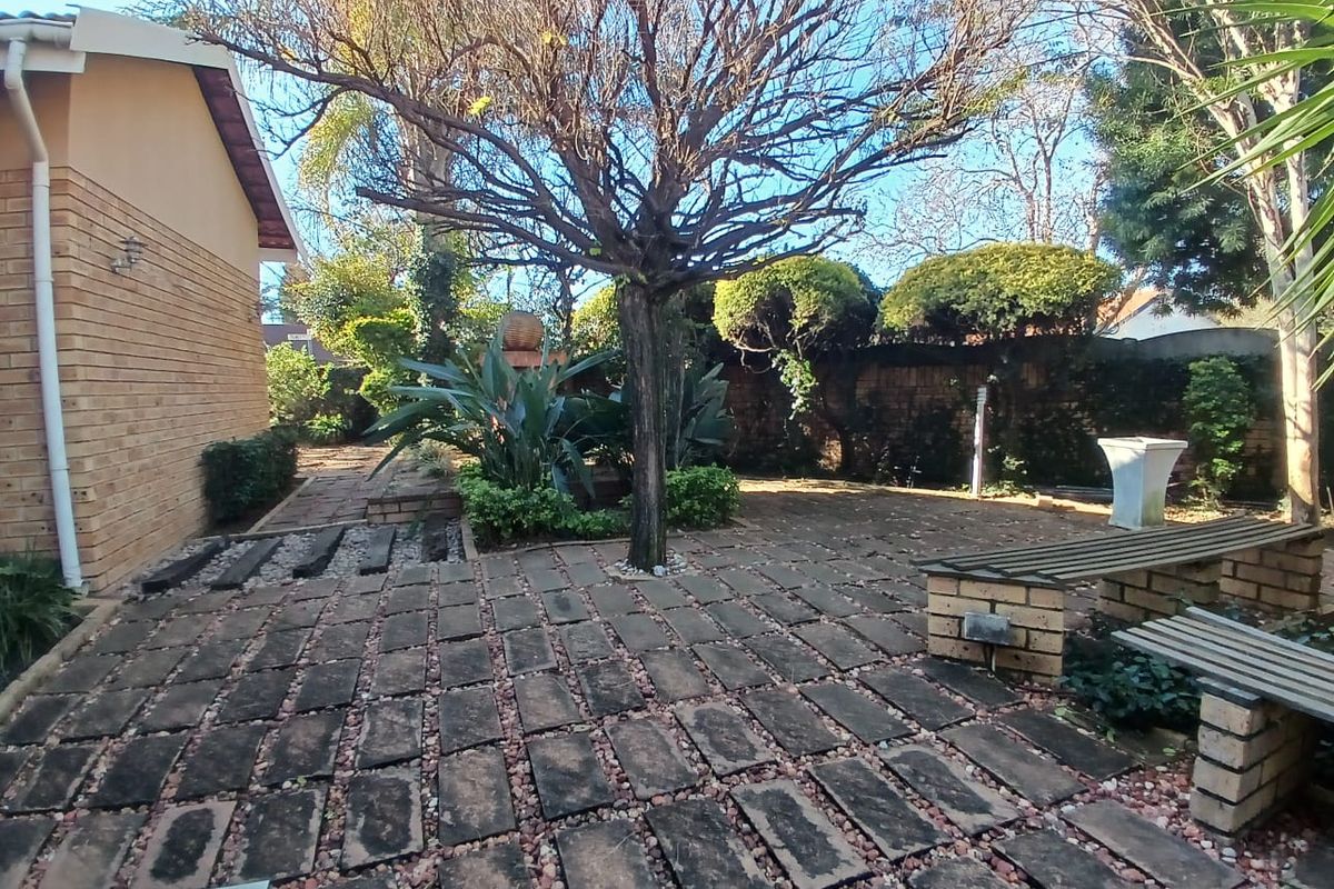 A private rear garden area featuring brick paving, established trees, and a built-in brick bench, offering a quiet outdoor space.