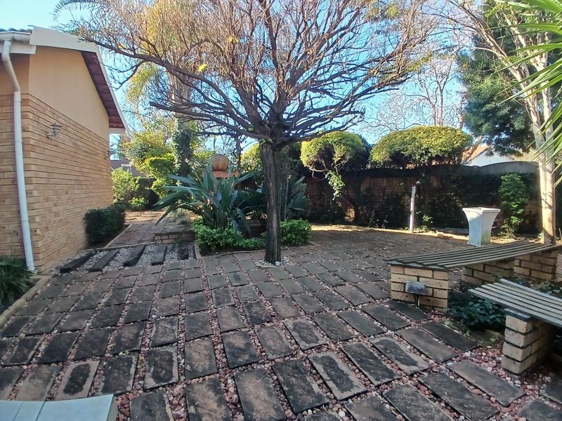 A private rear garden area featuring brick paving, established trees, and a built-in brick bench, offering a quiet outdoor space.