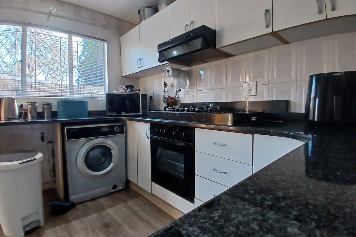 A functional kitchen featuring white cabinetry, dark granite countertops, a built-in oven with gas hob, and dedicated space for laundry appliances.