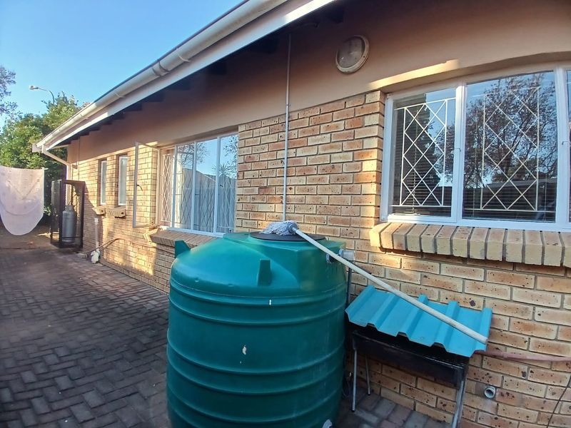 Rear exterior view of the apartment featuring face brick walls, security-fitted windows, paved flooring, and a large water storage tank.