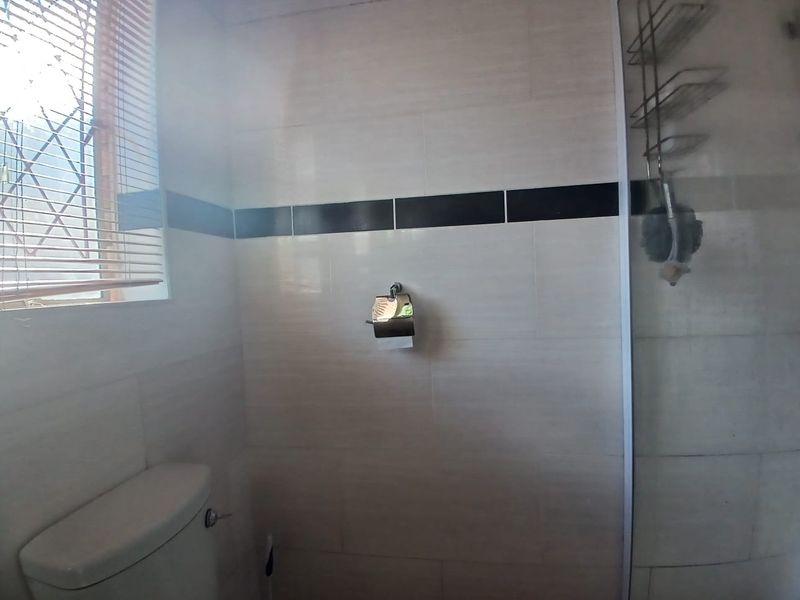 A functional bathroom featuring tiled walls with a decorative border, a shower enclosure, and a toilet.