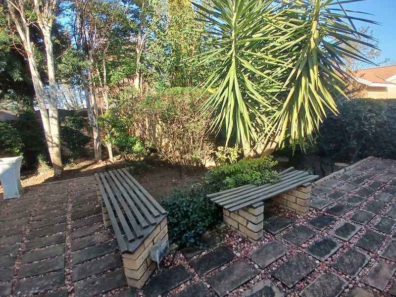 A landscaped garden area featuring a brick-paved patio with built-in brick benches surrounded by mature trees and established greenery.