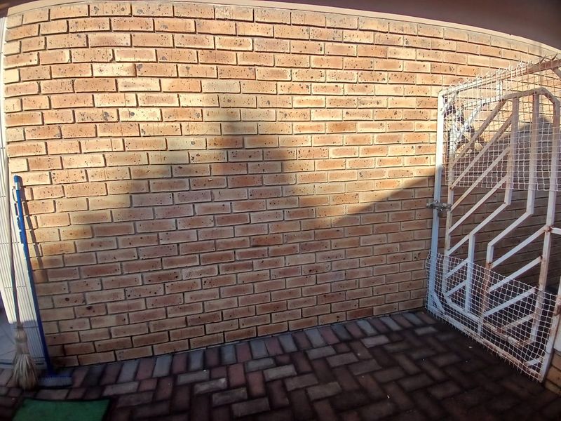 A rear exterior area featuring a face brick wall, paved flooring, and a metal security gate.