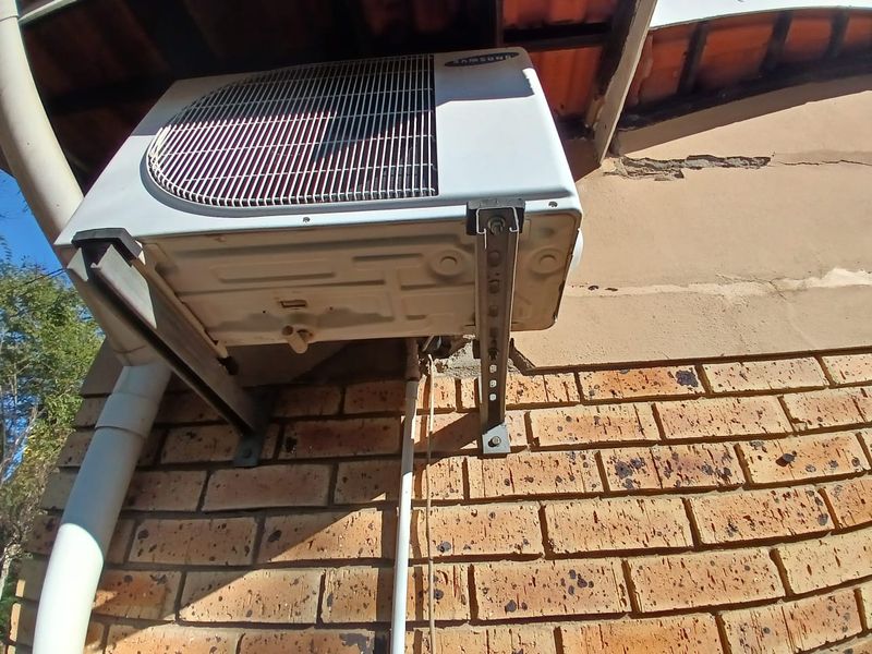 Exterior view of a wall-mounted air conditioning condenser unit installed on a brick facade showing signs of plaster cracking and masonry wear.