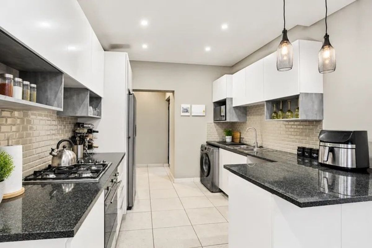 Modern kitchen featuring high-gloss cabinetry, granite countertops, subway tile backsplash, gas hob, built-in oven, and integrated laundry facilities in a clean, functional layout.