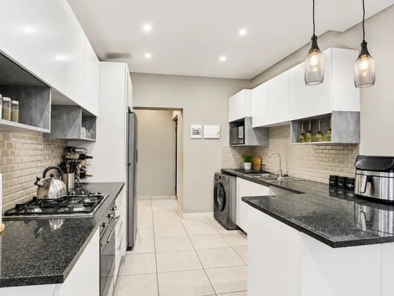 Modern kitchen featuring high-gloss cabinetry, granite countertops, subway tile backsplash, gas hob, built-in oven, and integrated laundry facilities in a clean, functional layout.