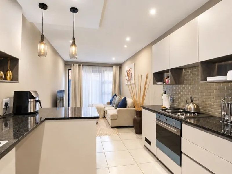 Modern open-plan kitchen and living area featuring sleek cabinetry, granite countertops, subway tile backsplash, and integrated appliances, leading to a bright lounge space.