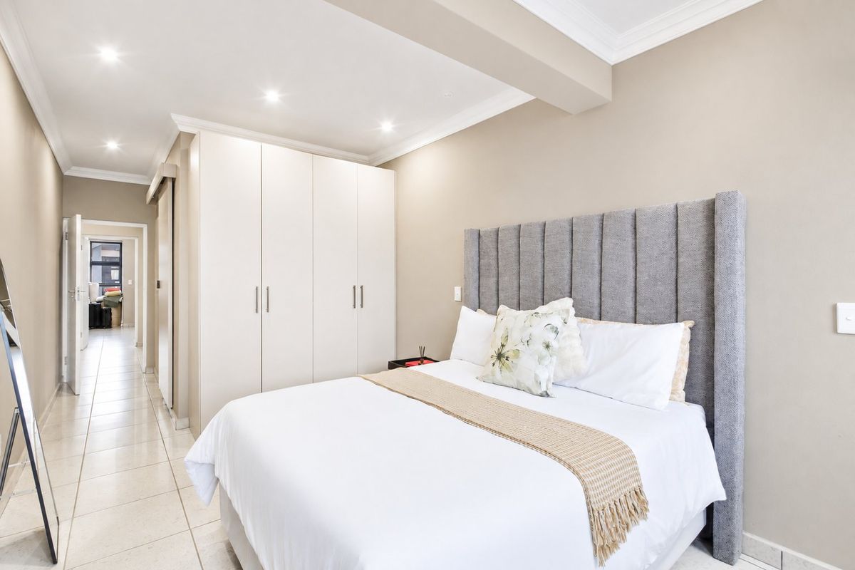 A well-maintained bedroom featuring neutral walls, tiled flooring, recessed downlighting, and ample built-in cupboard storage.