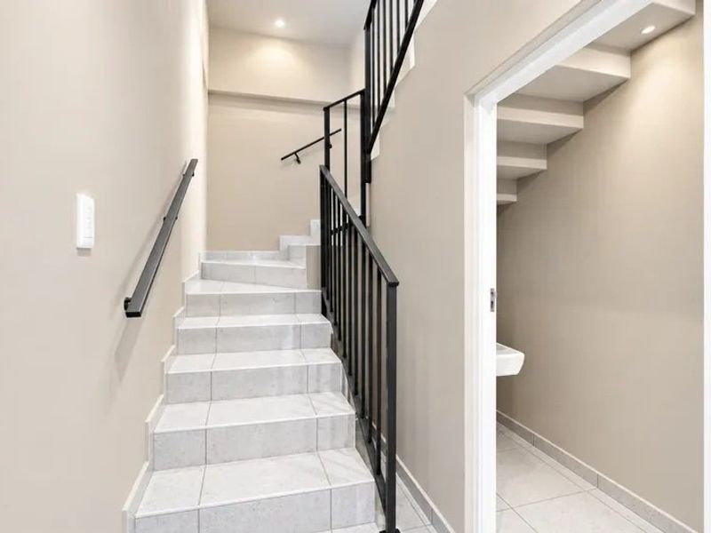 A clean, modern hallway featuring a tiled staircase with a black metal balustrade and a convenient under-stair storage space.