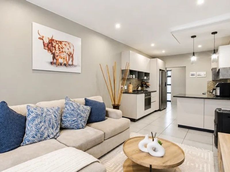 Modern open-plan living area featuring a sleek kitchen with stone countertops, built-in appliances, and tiled flooring, seamlessly flowing into the lounge space.