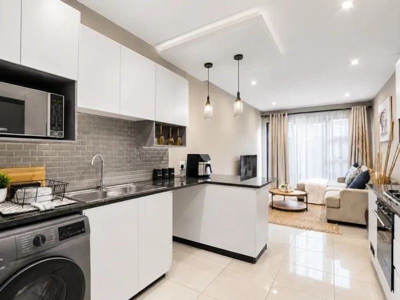 Modern open-plan kitchen and living area featuring sleek white cabinetry, subway tile backsplash, integrated appliances, and polished tiled flooring with contemporary lighting.