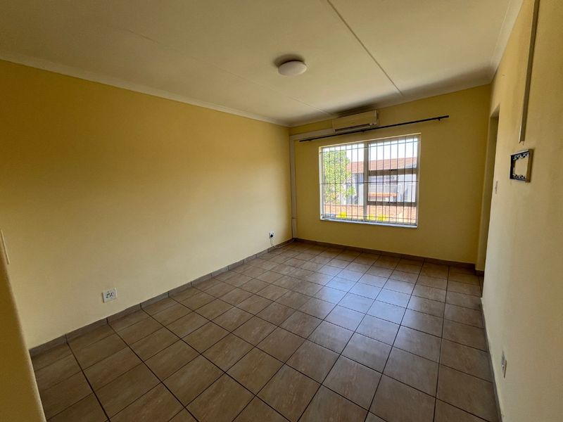 A vacant bedroom featuring tiled flooring, security bars on the window, and a wall-mounted air conditioning unit.