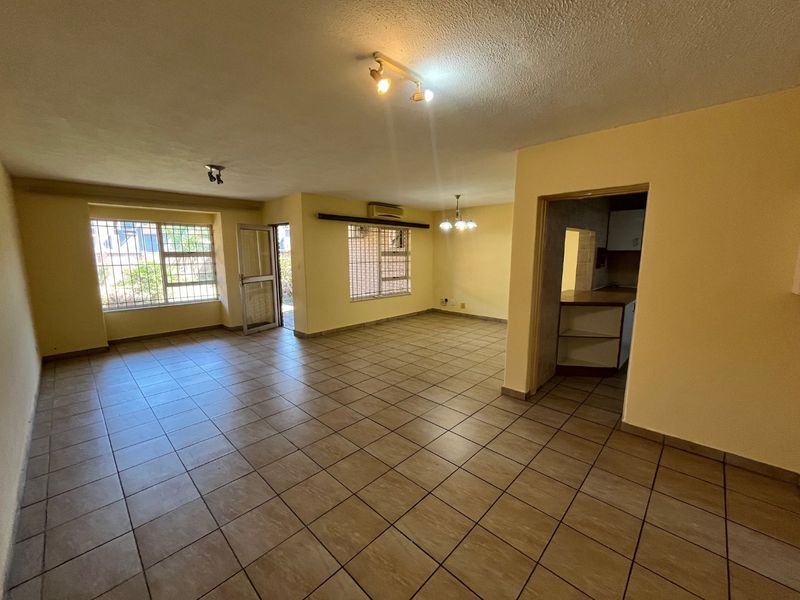 Spacious open-plan living and dining area featuring tiled flooring, security bars on windows, and an integrated air conditioning unit, leading into the kitchen.