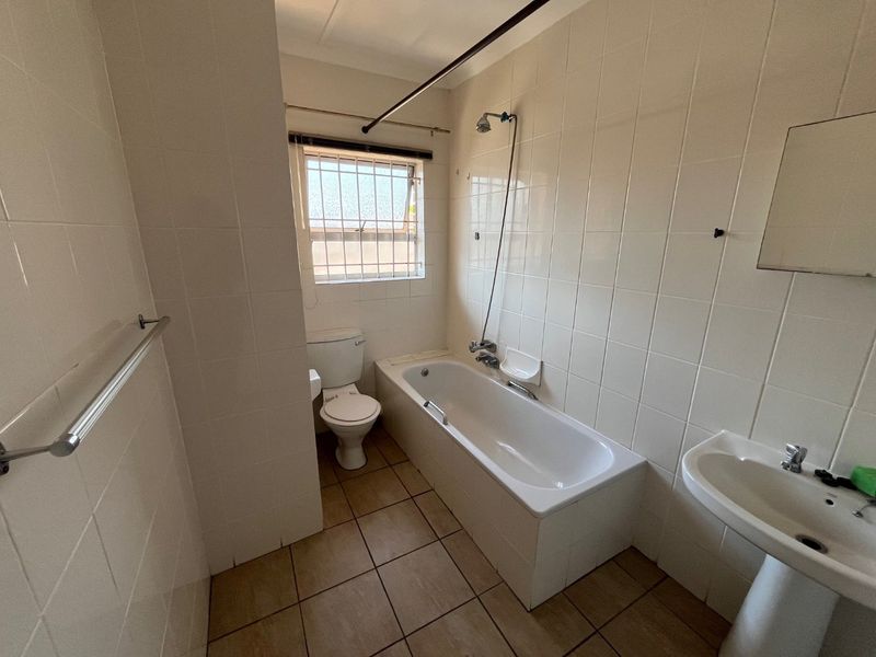 A functional bathroom featuring a bathtub with shower mixer, pedestal basin, and toilet, finished with neutral wall and floor tiles.