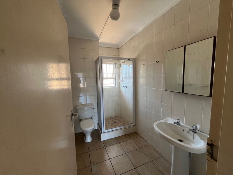 A functional bathroom featuring a pedestal basin, shower enclosure, and toilet, finished with full-height wall tiling and floor tiles.