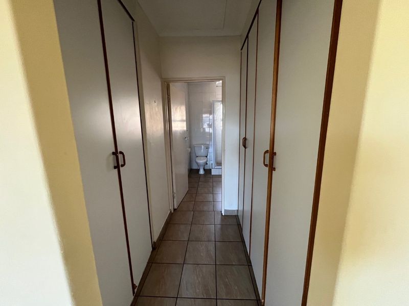 A functional hallway featuring extensive built-in cupboard storage and tiled flooring, leading directly into an adjacent bathroom.