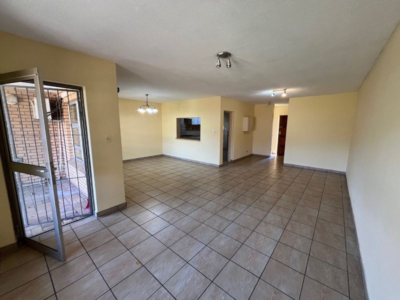 Spacious open-plan living area featuring neutral tiled flooring, a convenient pass-through window to the kitchen, and direct access to an outdoor patio area.