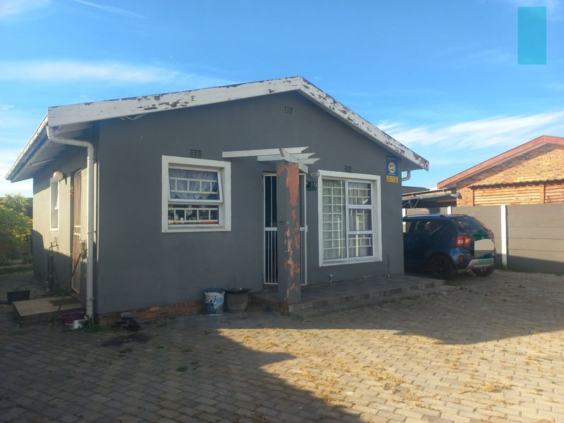 Front elevation of a detached house featuring a paved driveway, security gates, and aluminium window frames, showing signs of exterior maintenance requirements.