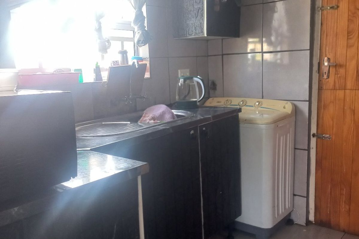 A functional kitchen area featuring built-in cabinetry, tiled splashbacks, and tiled flooring, with direct access to an adjacent room via a wooden door.