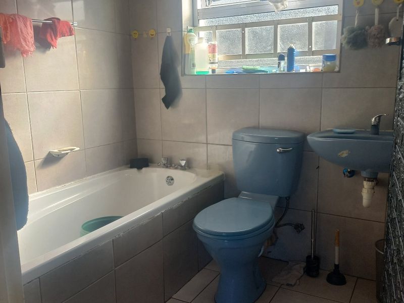 A compact bathroom featuring dated blue sanitaryware, including a bathtub, toilet, and wall-mounted basin, finished with neutral wall and floor tiling.
