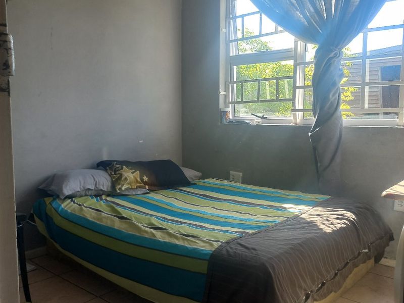 A compact bedroom featuring tiled flooring, security bars on the window, and a central pendant light fixture.